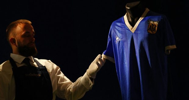 A Sotheby's technician adjusts a football shirt worn by Argentina's Diego Maradona during the 1986 World Cup quarter-final match against England, during a photocall at Sotheby's auction house in London on April 20, 2022, ahead of its sale. - The jersey worn by Diego Maradona when he scored twice against England in the 1986 World Cup, including the infamous "hand of God" goal, is to be auctioned off this month, Sotheby's announced Wednesday. The blue number 10 shirt has been owned since the end of the controversial World Cup encounter by opposing midfielder Steve Hodge, who swapped his jersey with Maradona after England lost 2-1. (Photo by ADRIAN DENNIS / AFP)
